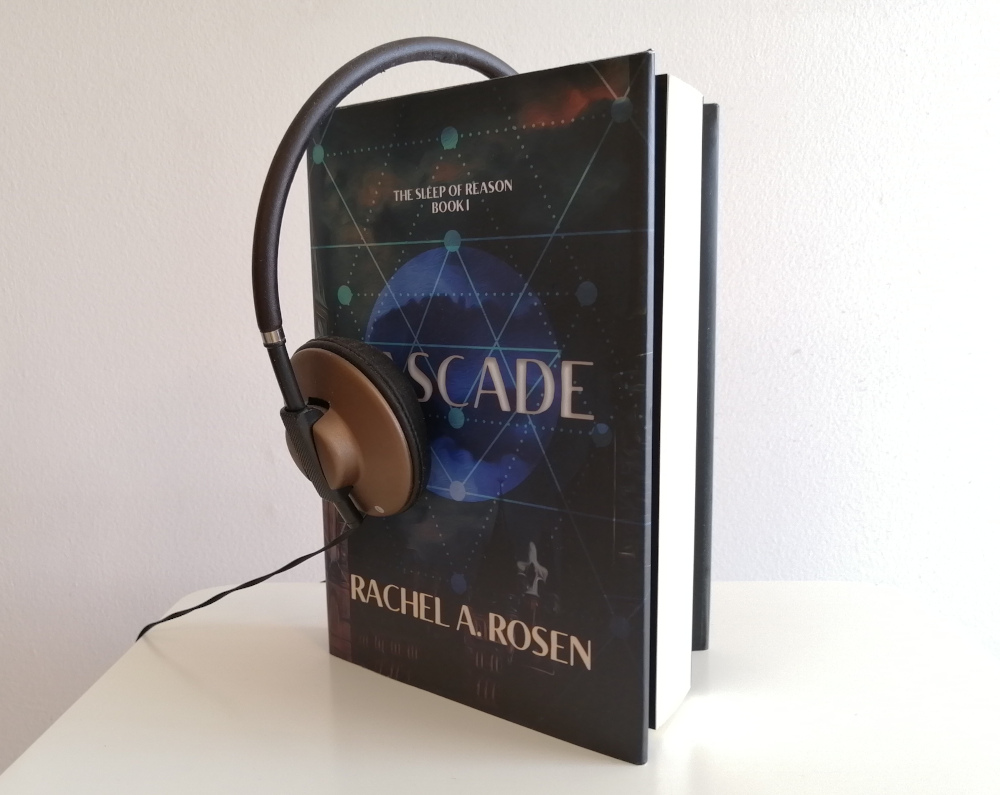 Image shows hard-cover copy of Cascade with earphones draped atop it, one earphone covering part of the front cover.