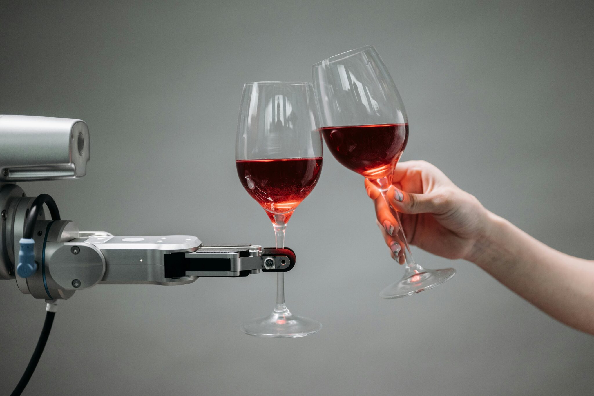 Image shows robot arm holding a glass of red wine on the left, toasting a human's arm also holding a glass of red wine. Image taken from the Wizards and Spaceships website.